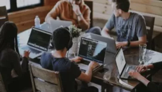 four people sitting at a desk working on laptops