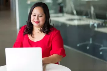 a woman in a bright red dress works on a laptop