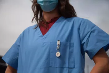 a nurse in blue with a watch and facemask